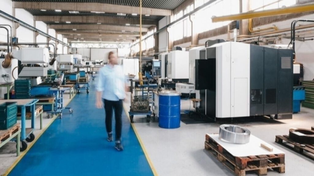 Person geht durch eine industrielle Produktionshalle mit moderner Maschinen- und Anlagentechnik.